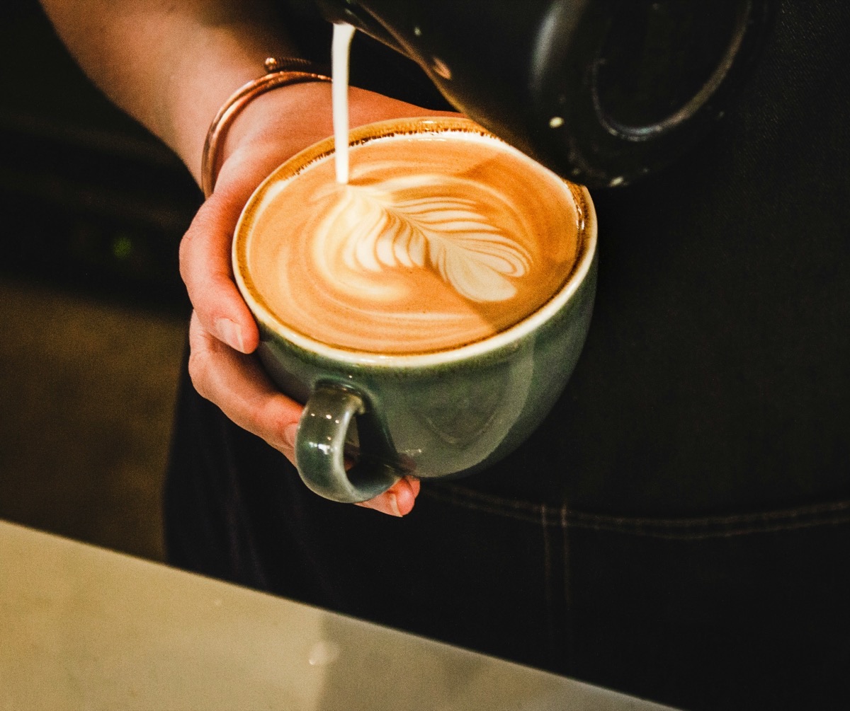 Hands pouring fresh coffee from a pitcher into a white cup