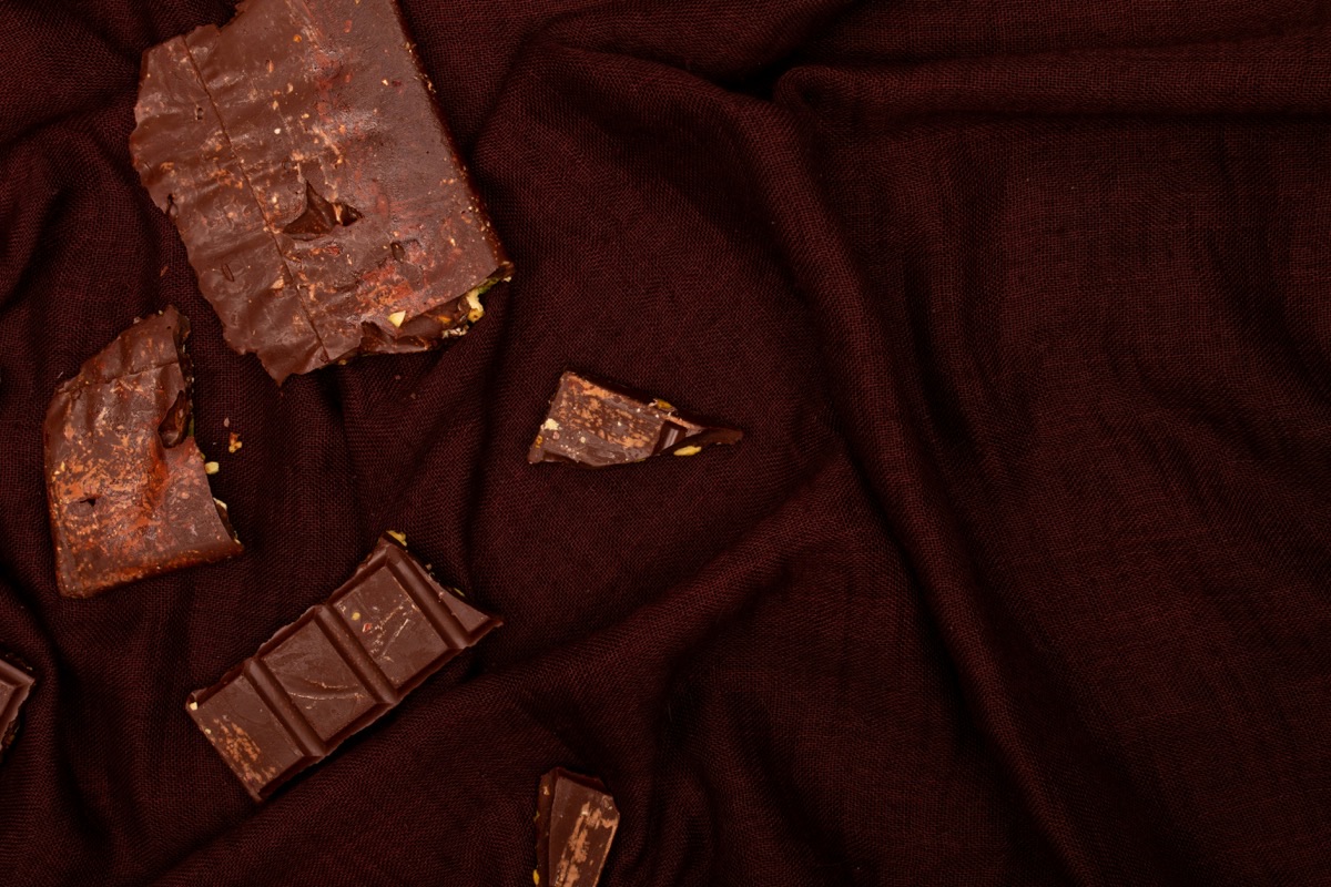 Broken pieces of dark chocolate arranged on a dark cloth, top view